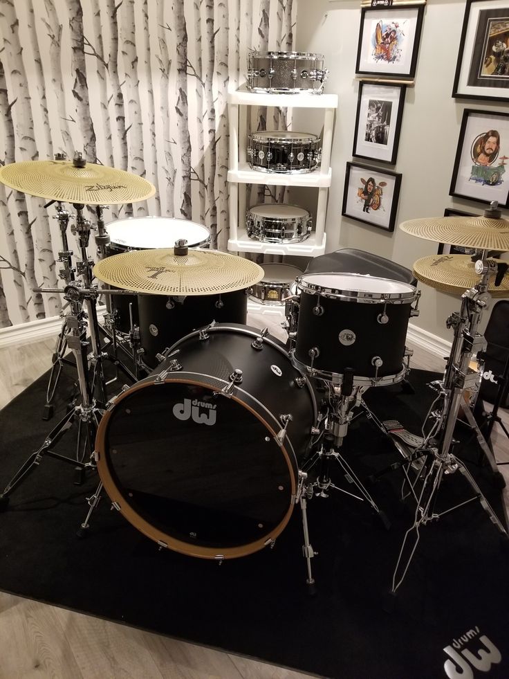 a drum set sitting on top of a black rug in front of a wall with pictures