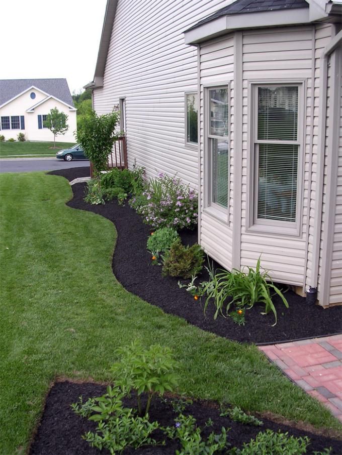 a house with grass and flowers in the front yard, next to a brick walkway