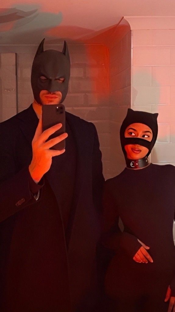 two people dressed up as batman and catwoman, one holding a cell phone to take a selfie