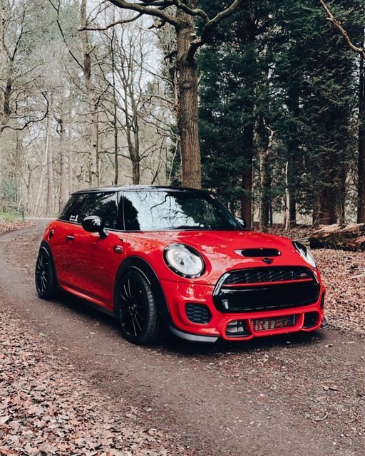 a red mini cooper driving down a forest road