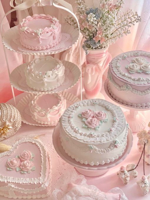 a table topped with lots of cakes covered in frosting and pink icing next to vases filled with flowers