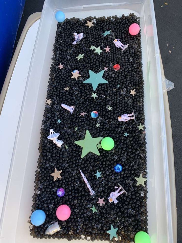 a plastic container filled with lots of black beads and stars on top of white tray