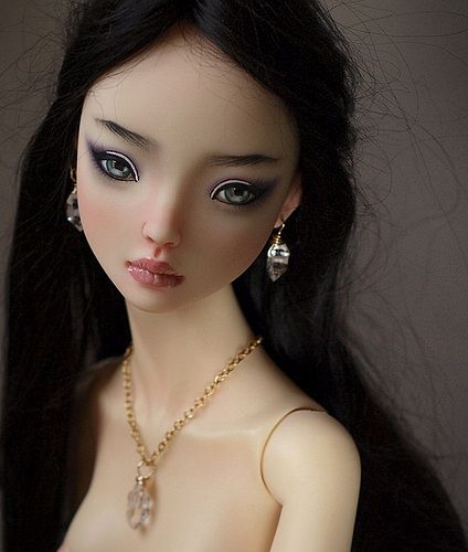 a close up of a doll wearing a necklace and earrings