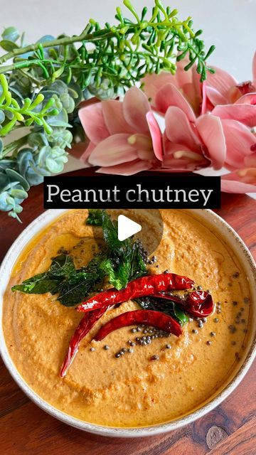 a bowl of peanut chutney with red chili peppers and green leaves on top