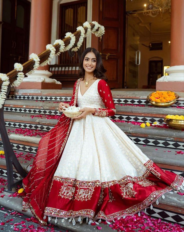 a woman in a white and red wedding dress standing on steps with flowers around her