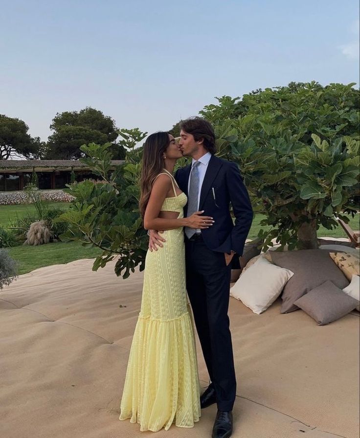 a man in a suit and tie kissing a woman in a yellow dress on the beach