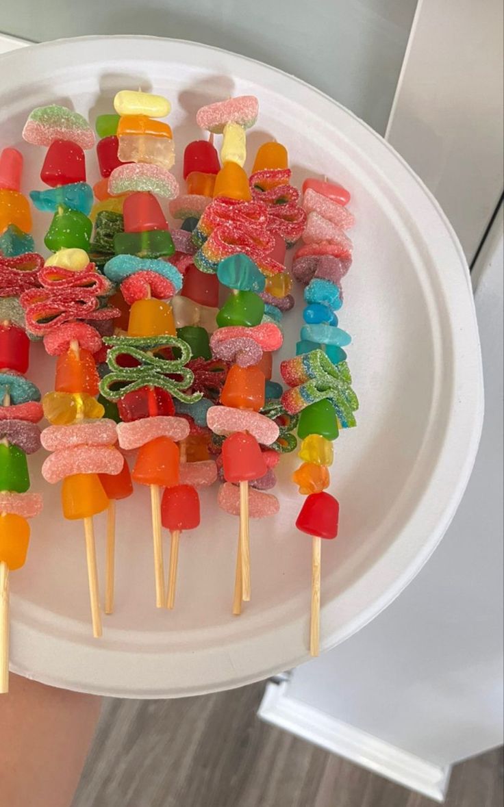 a person holding a white plate with many different colored lollipops on it