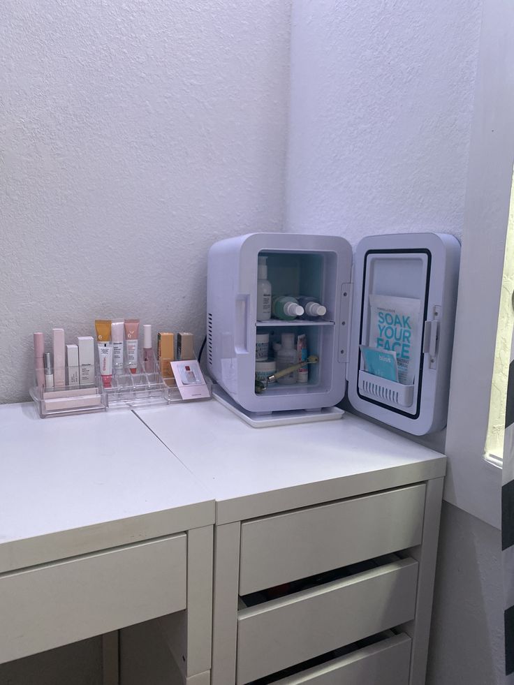 a small refrigerator sitting on top of a white counter next to a drawer filled with bottles