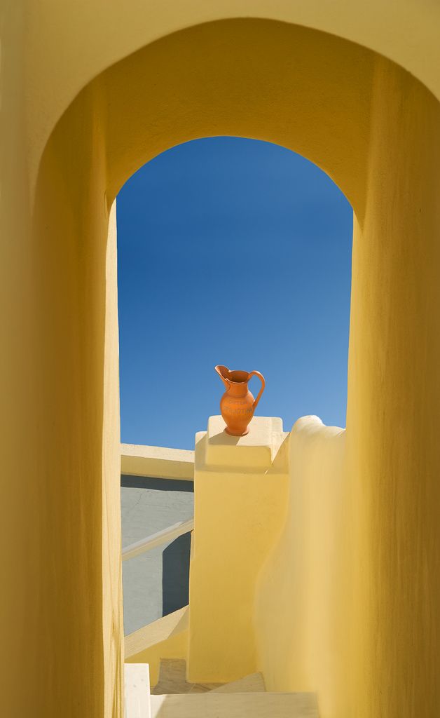 an orange vase sitting on top of a white wall next to stairs with blue sky in the background