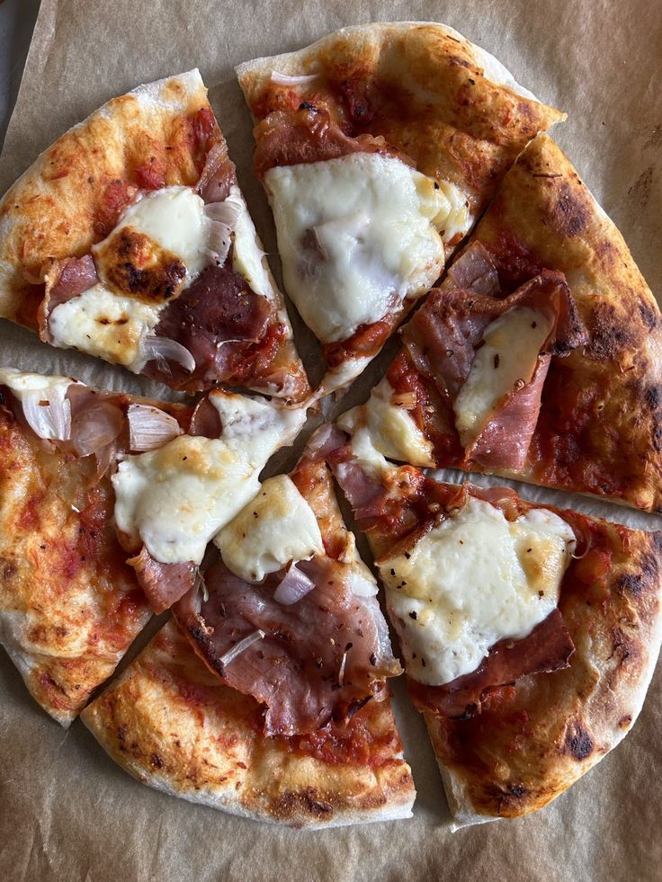 a pizza with cheese, ham and onions cut into eight slices on a piece of wax paper