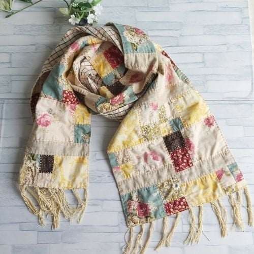 a multicolored patchwork scarf with fringes and flowers sitting on a white brick wall