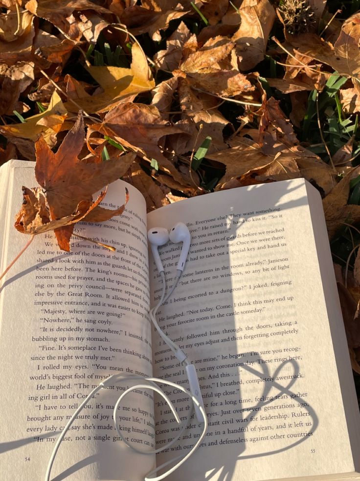 an open book with headphones laying on top of it in the grass next to leaves