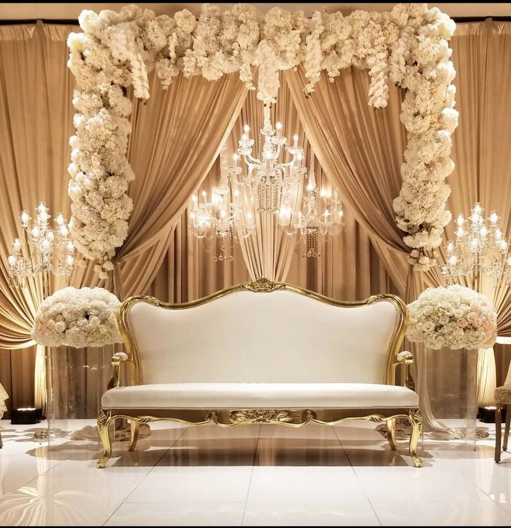 a white couch sitting under a chandelier next to a table with flowers on it