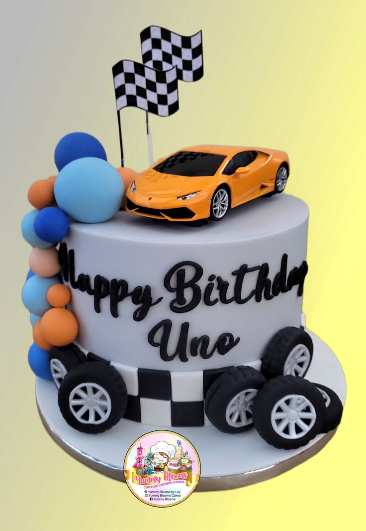 a birthday cake with a car on top and balloons in the shape of race cars