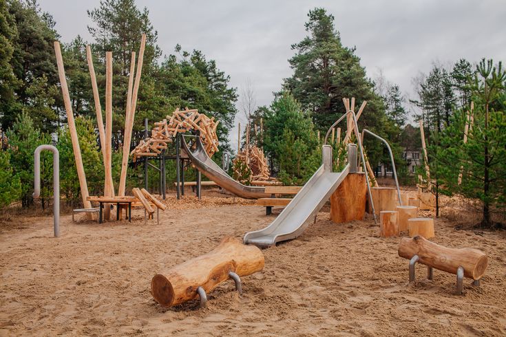 an empty playground in the middle of some trees and sand with swings, slides and benches