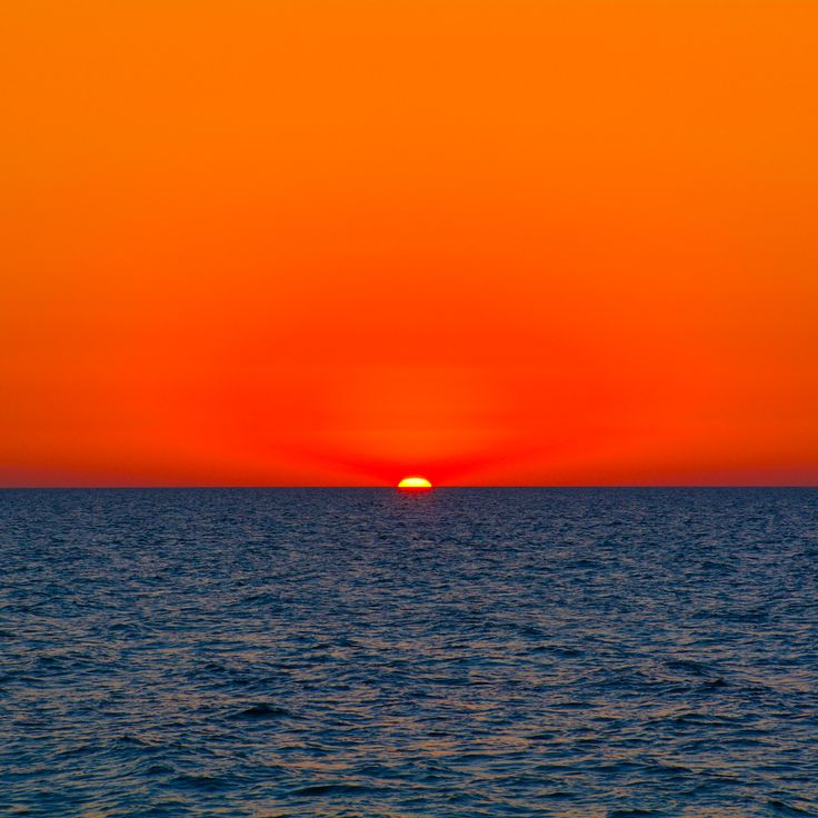 the sun is setting over the ocean on an orange and blue sky day or night