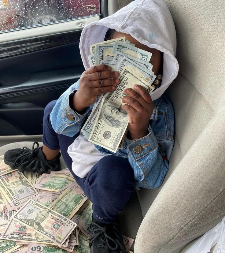 a little boy sitting in the back seat of a car holding money up to his face