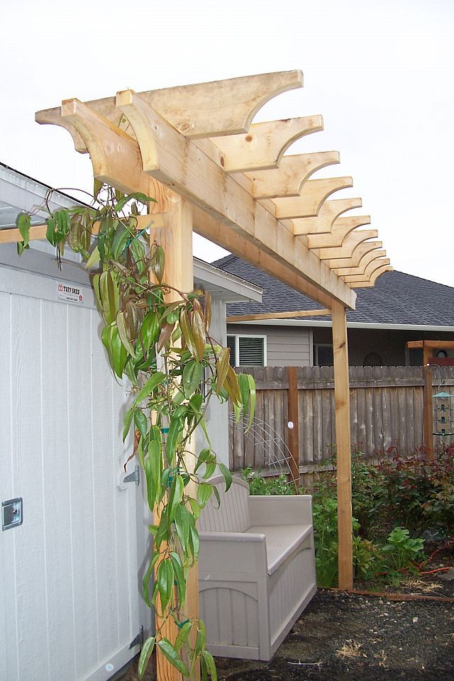 a wooden pergolan sitting on top of a yard next to a building with a bench under it