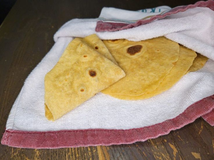 two tortillas are wrapped in a towel on a wooden table with a red and white cloth