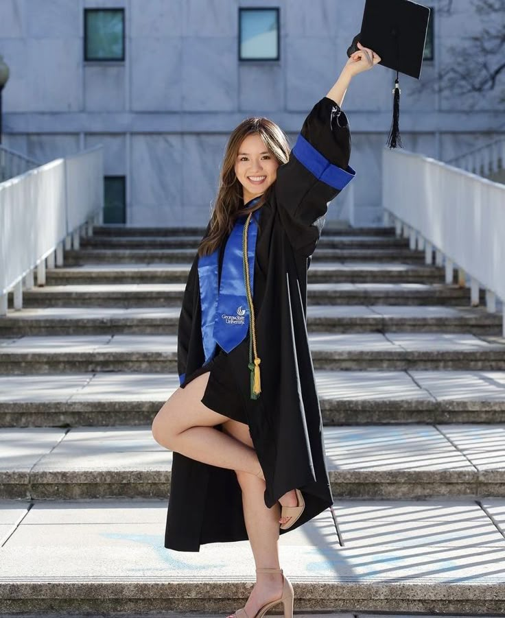 a woman in graduation gown holding up her cap and diploma while sitting on the steps