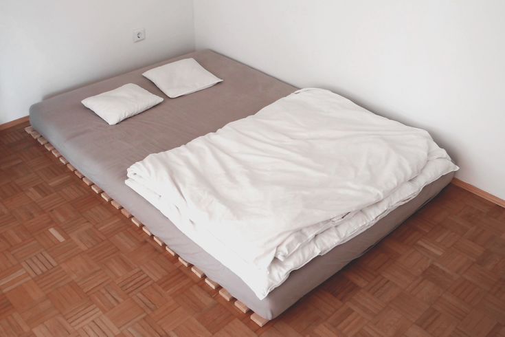 a bed sitting on top of a wooden floor next to a white wall in a bedroom