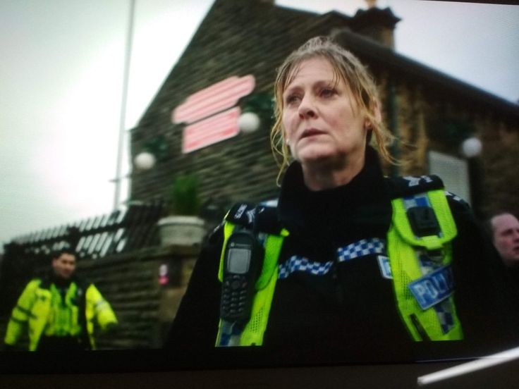 two police officers standing in front of a building with a woman on the screen looking off to the side