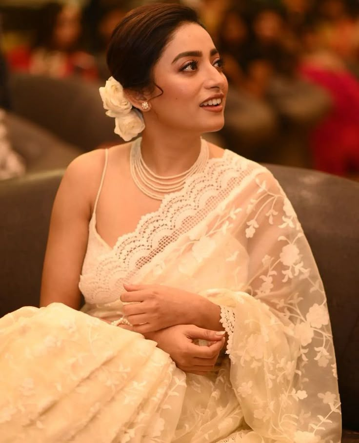 a woman sitting on top of a couch wearing a white dress and flower in her hair