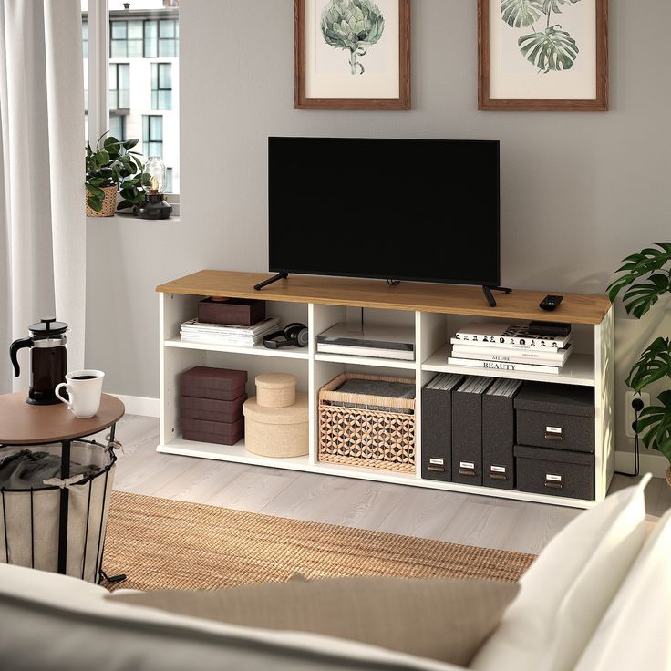 a flat screen tv sitting on top of a wooden shelf in a living room next to a window