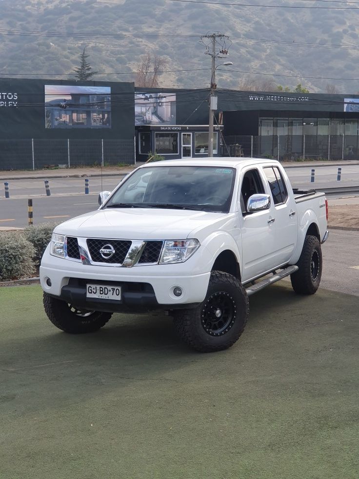 a white pick up truck parked in front of a building with mountains in the background