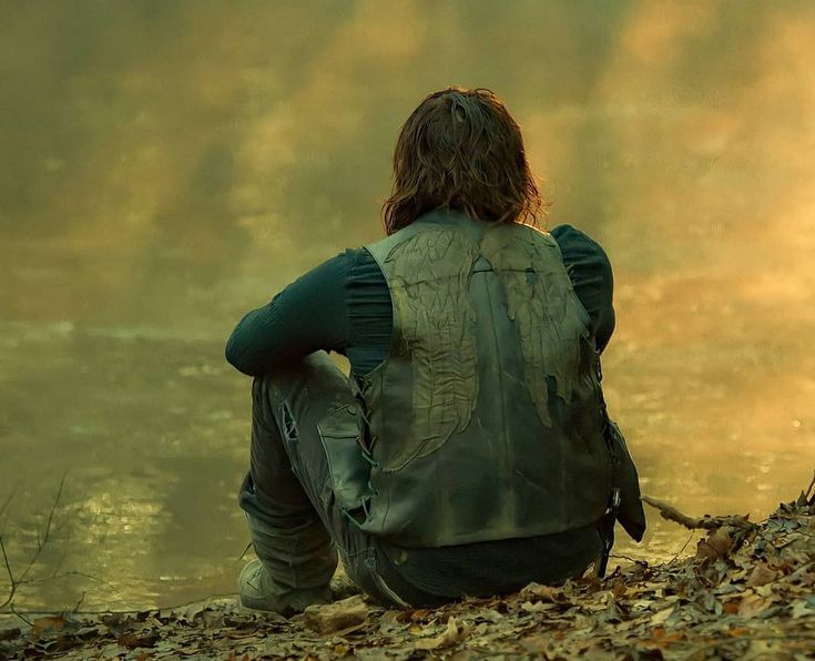 a person sitting on the ground next to a body of water with leaves all over it