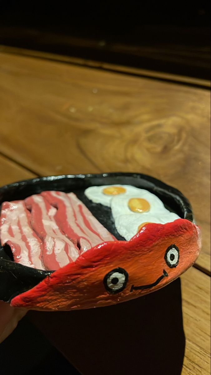 a person is holding up a plate with food in the shape of a fish and bacon on it