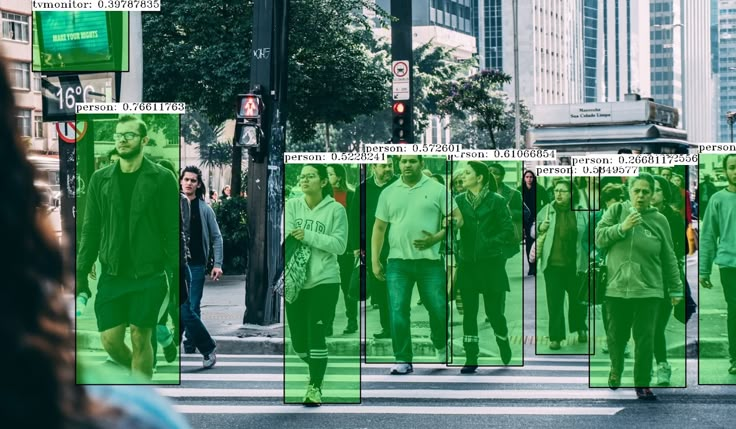 people walking across a crosswalk in the city, with green images on them and buildings behind them