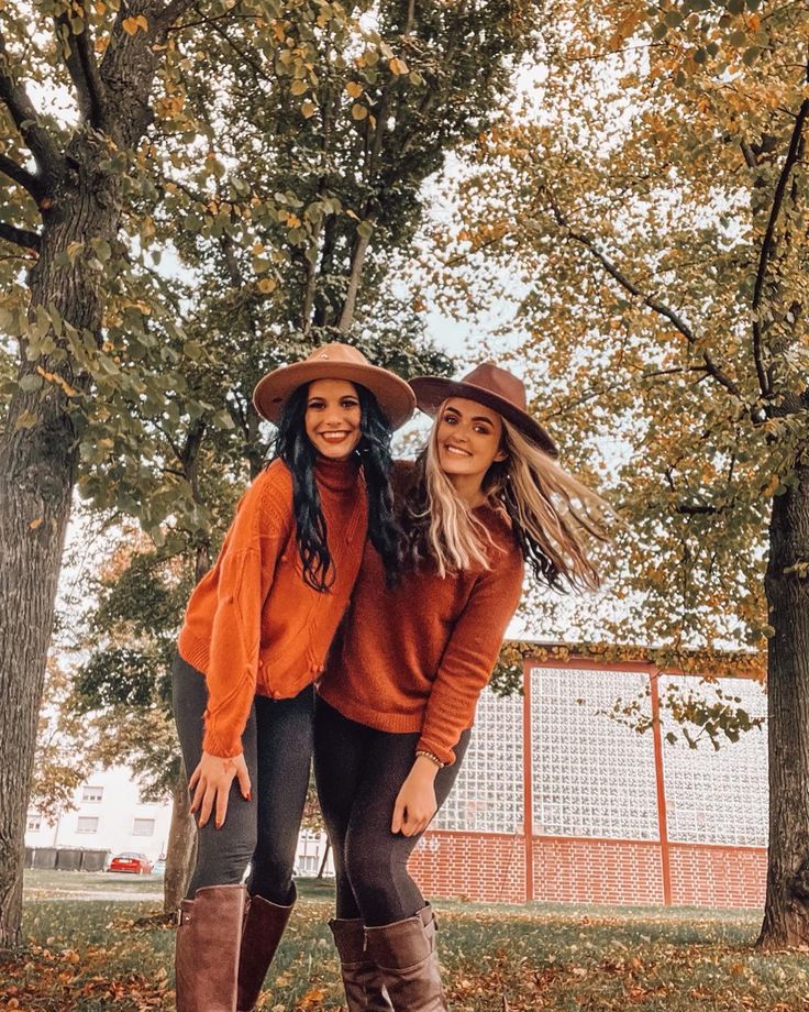 two young women standing next to each other in front of trees with leaves on the ground