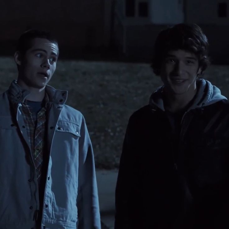 two young men standing next to each other in front of a dark building at night