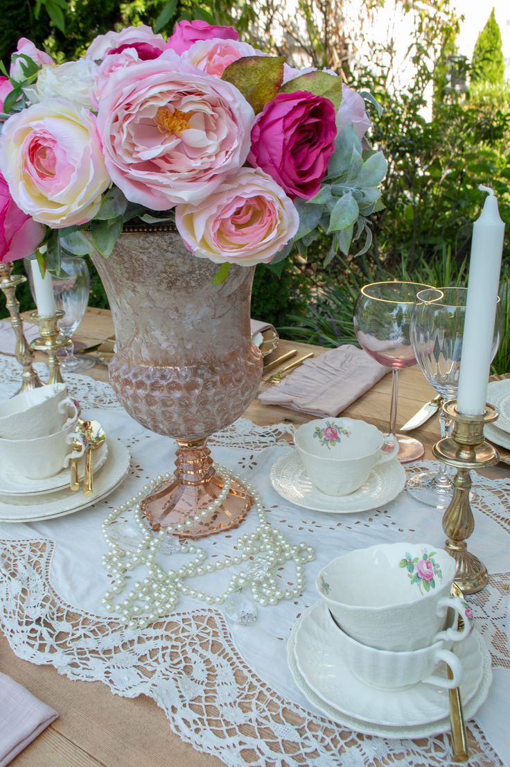 the table is set with pink roses and tea cups, gold candlesticks, and white china