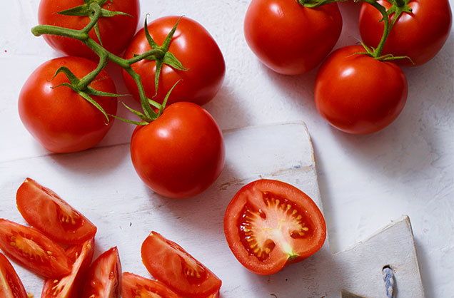 several tomatoes on a cutting board with a pair of scissors next to them and one half cut in half