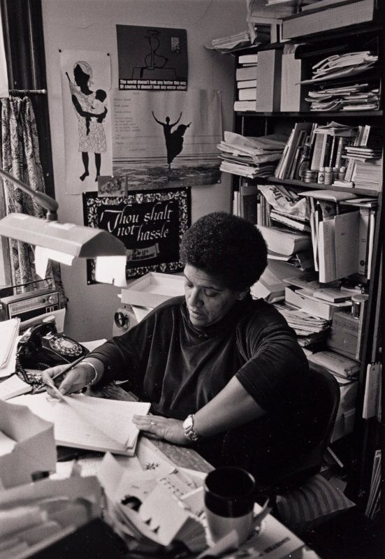 a woman sitting at a desk in front of a book shelf filled with books and papers