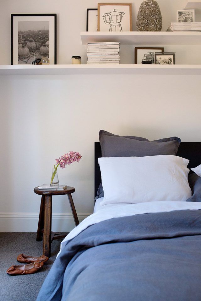 a bed with blue sheets and white pillows in a bedroom next to a shelf filled with pictures