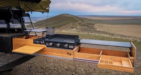 an outdoor kitchen is built into the back of a truck with mountains in the background