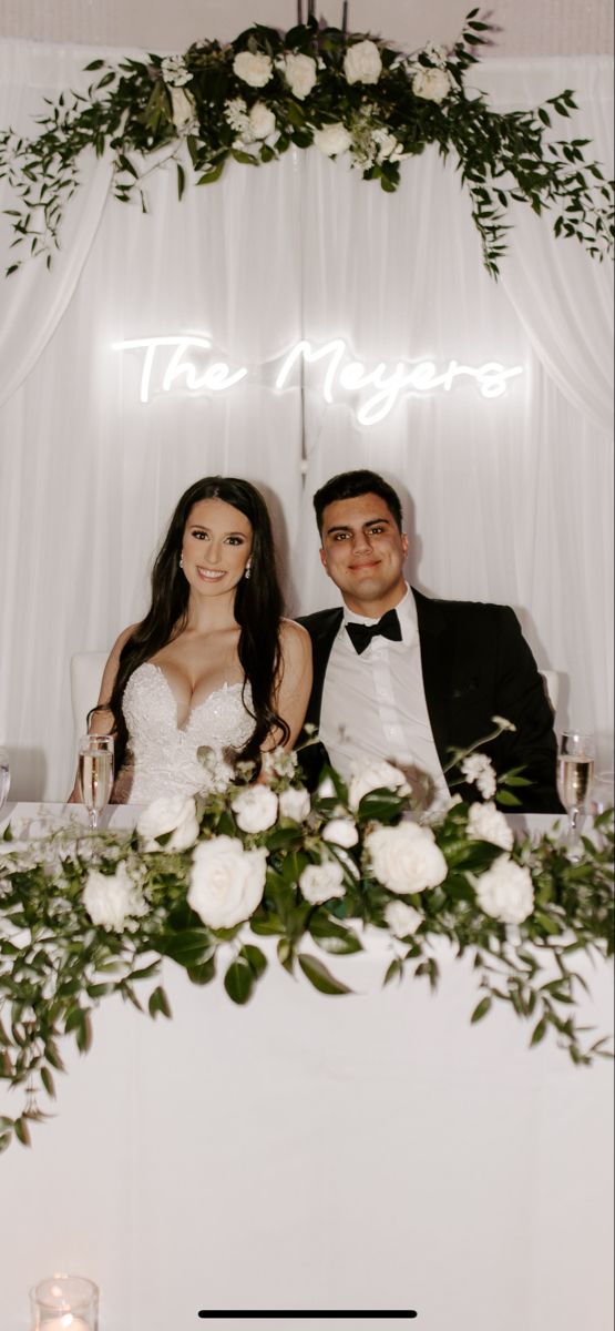 a man and woman sitting next to each other in front of a table with flowers