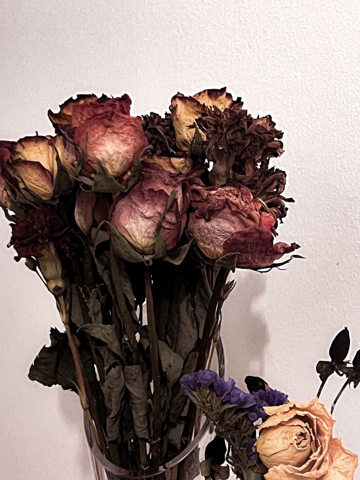 a vase filled with lots of flowers on top of a wooden table next to a white wall