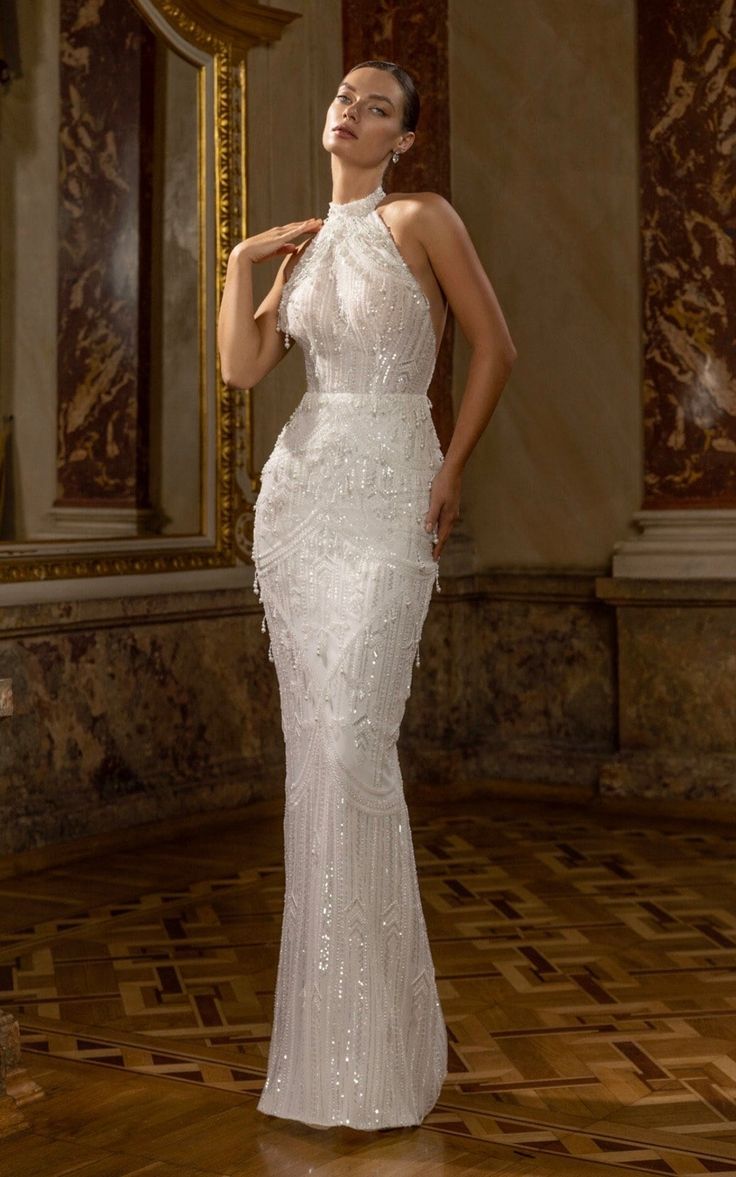 a woman in a white dress standing on a wooden floor with her hands behind her head