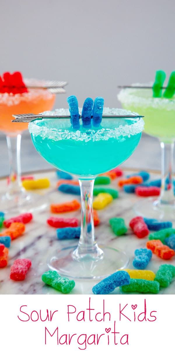 three glasses filled with different colored liquids on top of a marble table covered in gummy bears