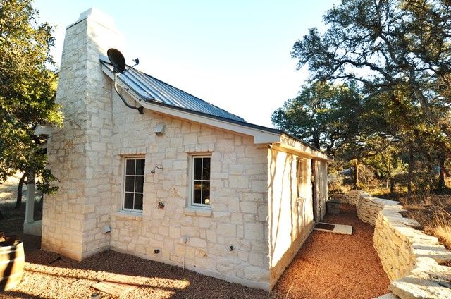 a small stone building with a metal roof and window on the side, next to a tree