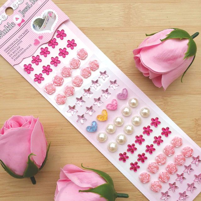 a pink rose next to a sticker sheet with hearts and flowers on it,