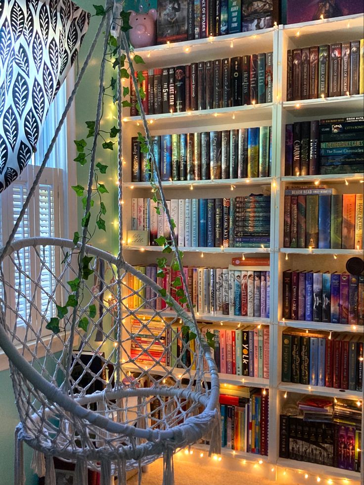 a book shelf filled with lots of books next to a window covered in fairy lights