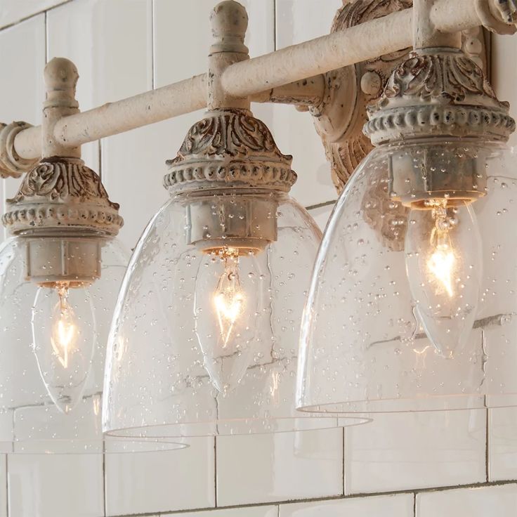 three clear glass globe lights hanging from a bathroom fixture