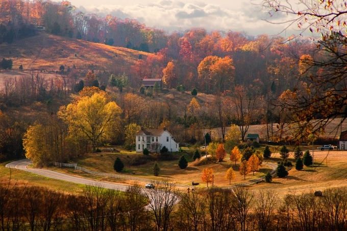 a white house sitting on top of a lush green hillside next to trees with orange and yellow leaves