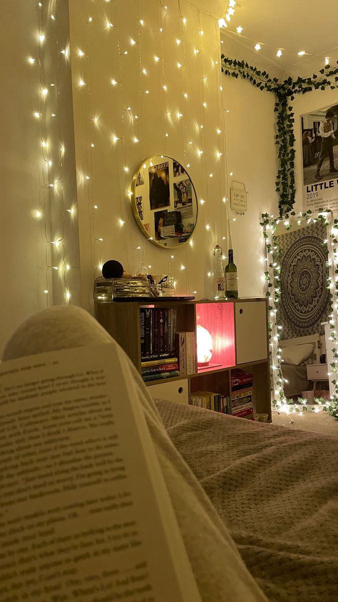 an open book sitting on top of a bed next to a wall covered in christmas lights