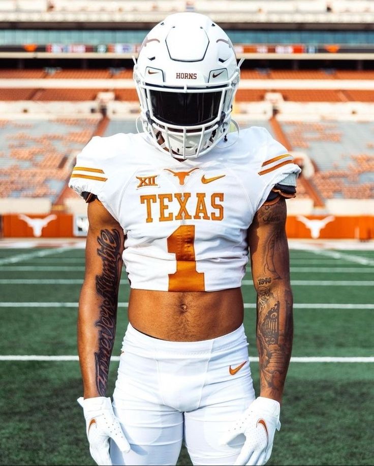 a football player with tattoos on his chest and in white uniform standing on the field